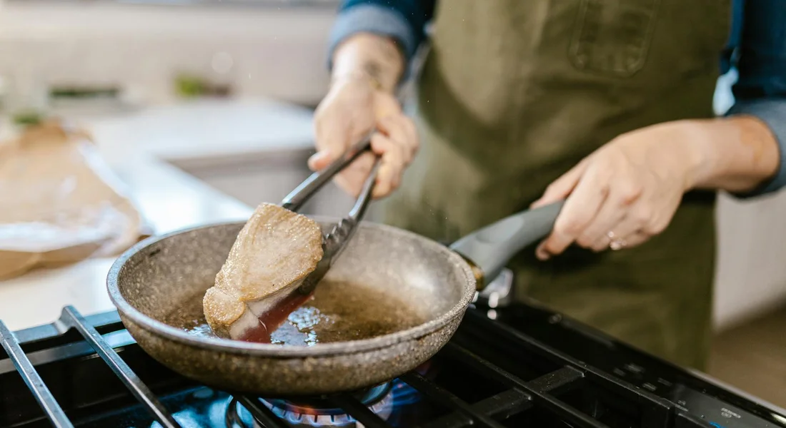 A cook uses tongs to place a piece of ahi tuna into a hot cast-iron skillet on a gas stove.