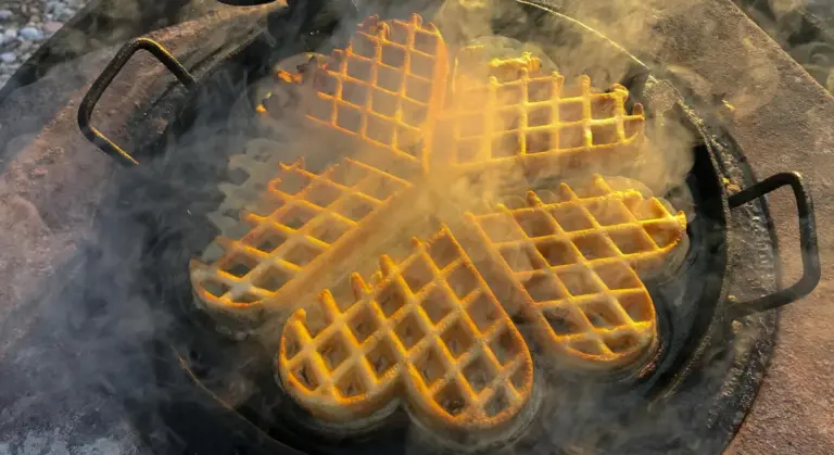 Cast iron pan with a four-quadrant waffle pattern on a hot grill, with flames and smoke rising around it.