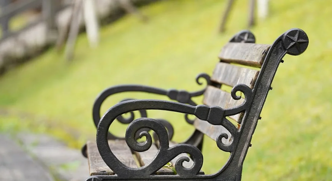 Outdoor park bench with ornate metal arms, representing routine preventive cleaning for outdoor furniture.
