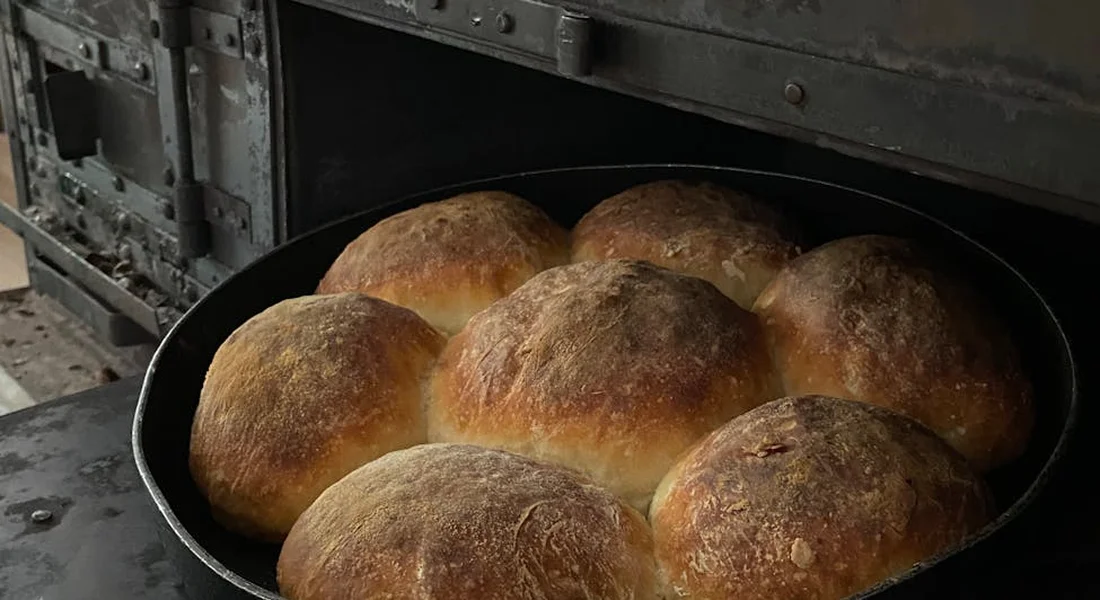 Crusty round bread loaves baking in a large cast-iron skillet on a stove.
