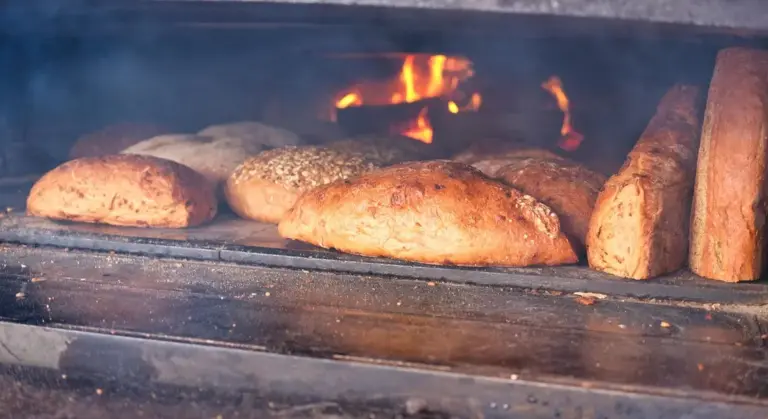 Loaves of bread baking inside a wood-fired oven with visible flames