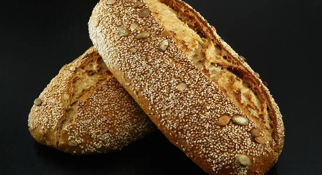 Two sesame-seeded crusty loaves on a dark surface