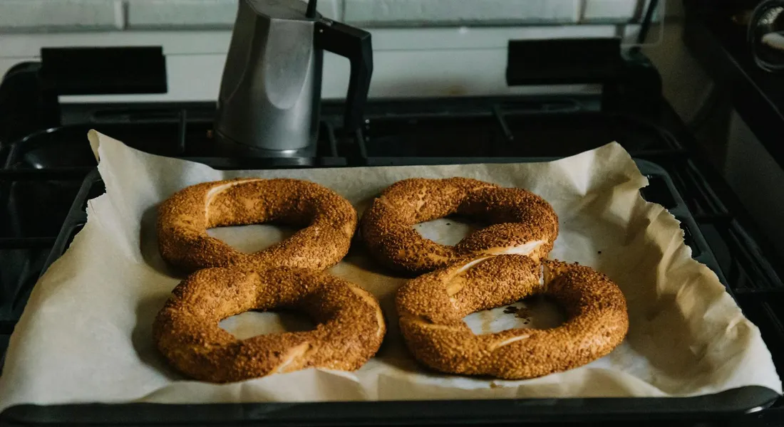 Four sesame-covered ring-shaped breads resting on parchment inside a cast iron Dutch oven on a stove.