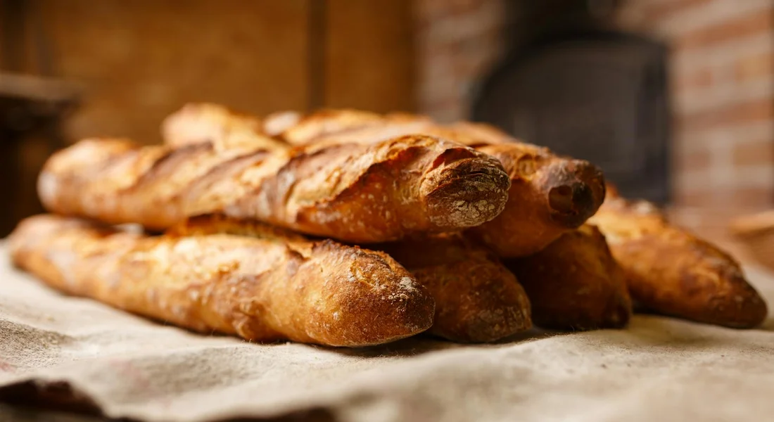 Stack of crusty bread loaves on a parchment-lined surface in a rustic kitchen.