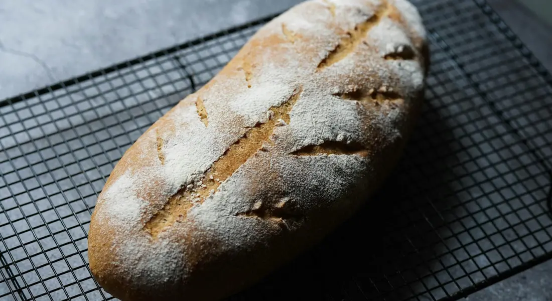 Loaf of bread cooling on a wire rack dusted with flour, suggesting kitchen maintenance and seasoning for cast iron cooking.