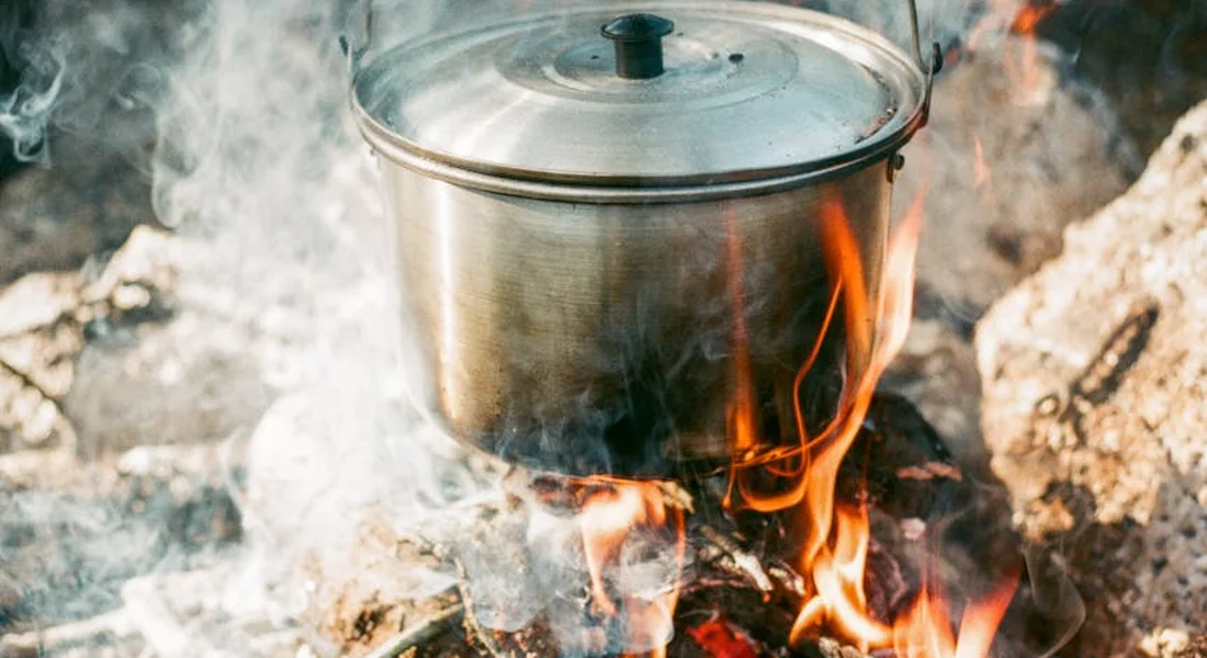 Cast iron pot over an open campfire with flames and smoke