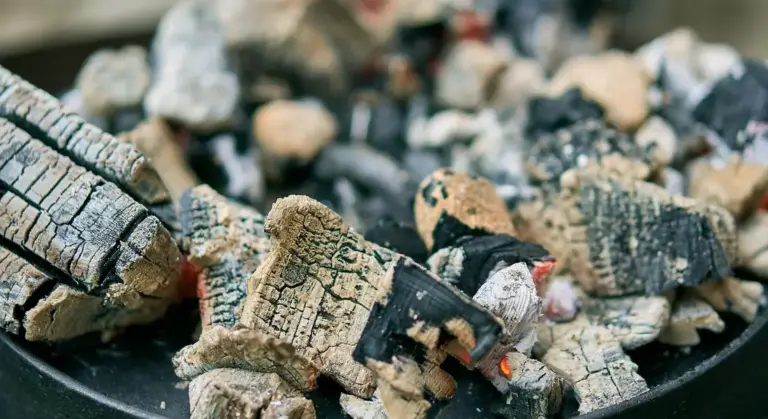 Close-up of glowing charcoal and embers on a campfire grill with charred wood