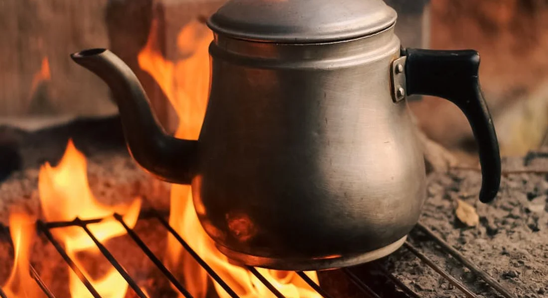 Cast iron kettle resting on a campfire grate with bright flames in the background
