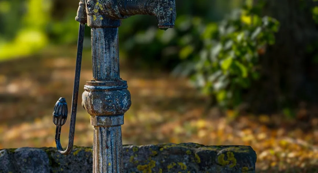 Close-up of a weathered cast-iron outdoor water pump with blue patina and moss, showing bare iron surface.