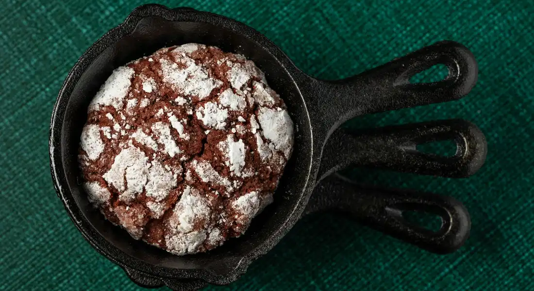Cast iron skillet with a powdered-sugar-dusted chocolate brownie resting on a dark green textured surface