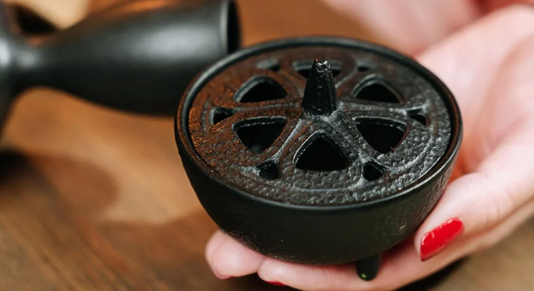 Close-up of a round cast-iron cooking piece with rust spots, held by a person with red-painted nails