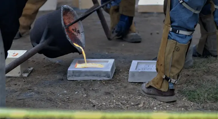 Worker pours molten iron into rectangular sand molds placed on the ground for cast iron cookware casting, with protective gear and boots visible.