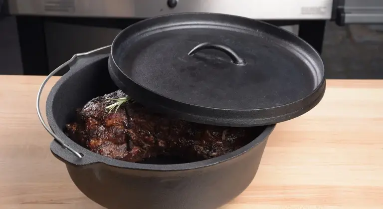 Cast iron Dutch oven with lid ajar on a wooden counter, showing a roasted dish with herbs inside
