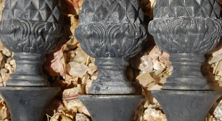 Close-up of decorative cast iron fence finials with intricate patterns, set against a background of dried autumn leaves.