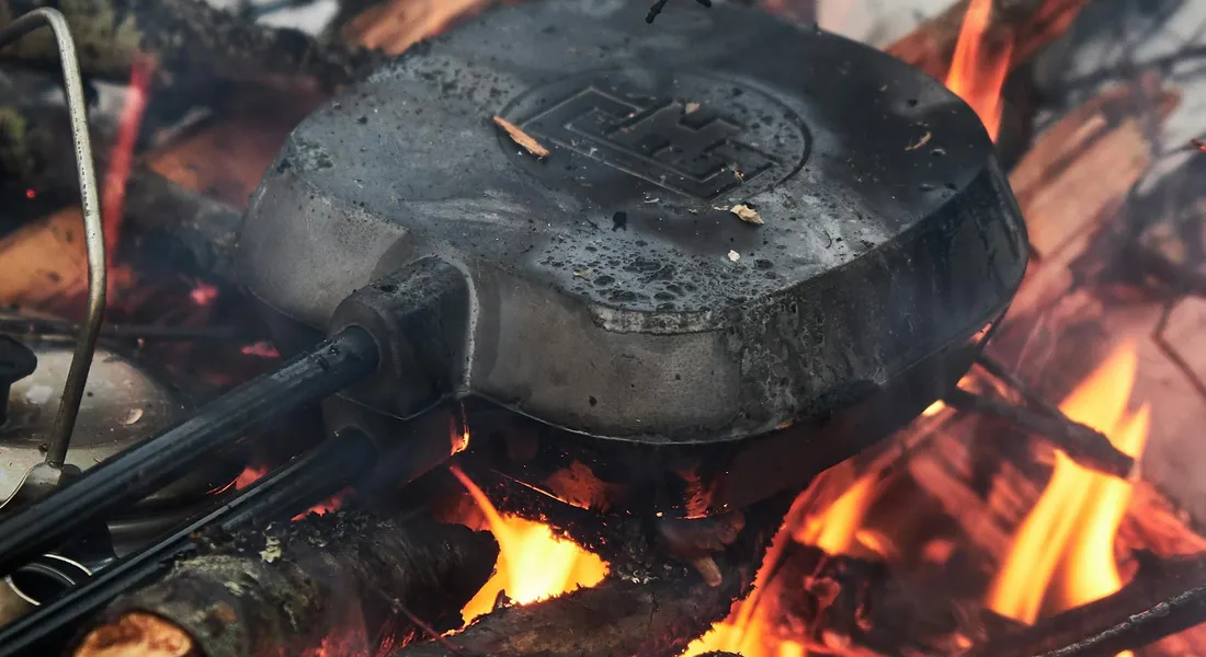 Round cast iron lid resting on glowing coals with flames in a grill.
