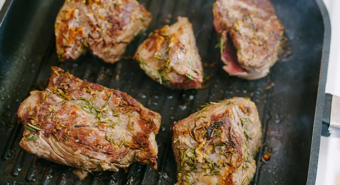 Beef steaks seared on a cast-iron grill pan with herbs, showing a crispy crust on the grill ridges.