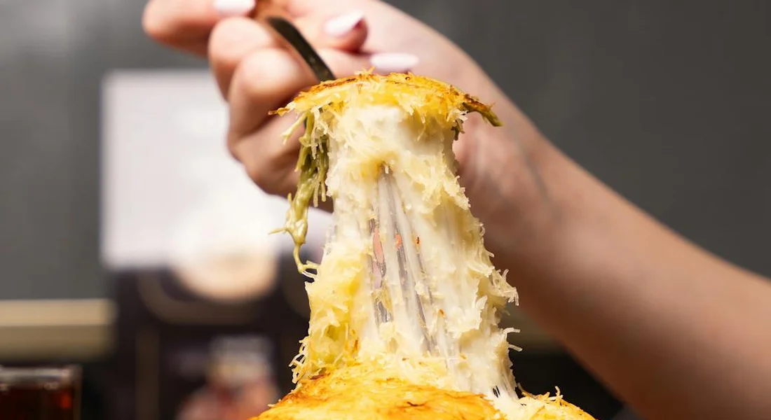 Close-up of a hand pulling a stringy cheese pull from a hot dish, highlighting melted cheese and the lingering heat.