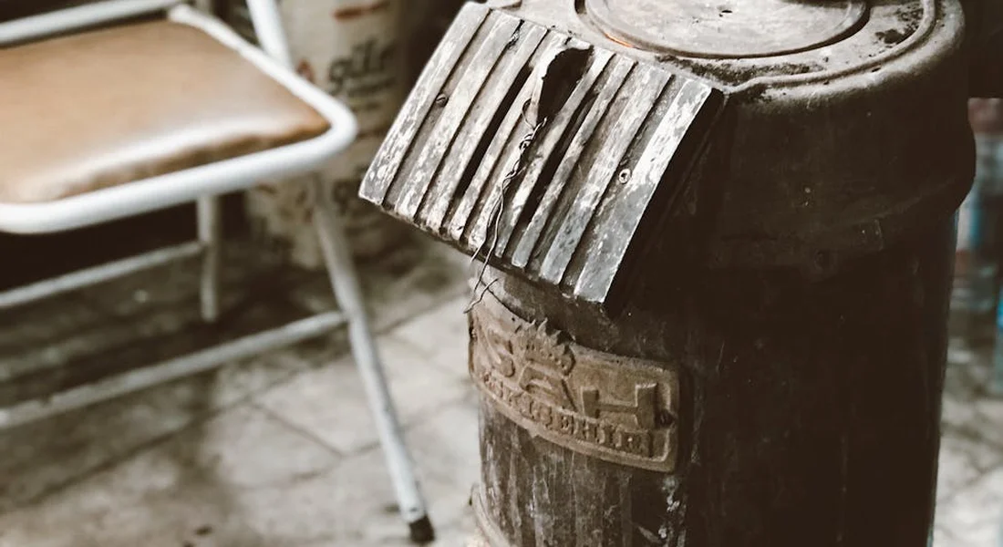 Close-up of a weathered metal drum with a ribbed lid in a workshop, with a brush resting on top.