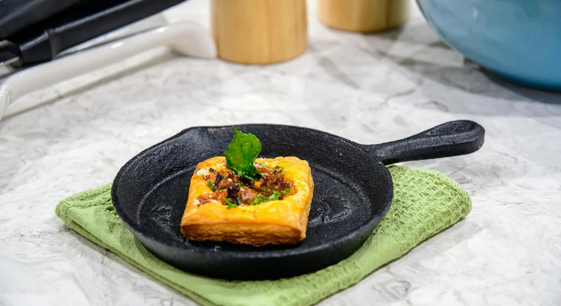 Cast iron pan holding a small square pastry on a green cloth, set on a marble countertop