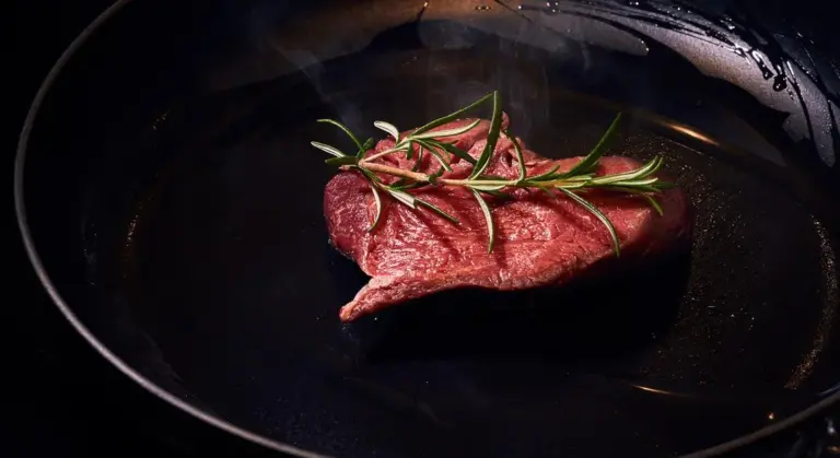 Raw steak in a hot cast-iron skillet with a sprig of rosemary on top