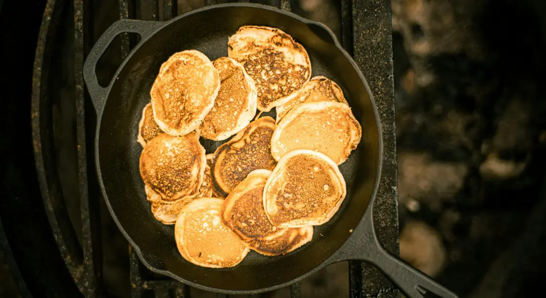 Cast iron skillet filled with golden-brown pancakes cooking on a stove.