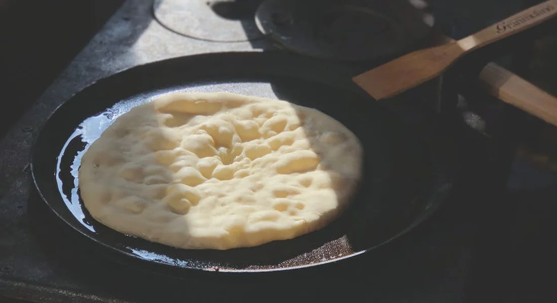 Pizza dough in a cast-iron skillet on a stove, with a wooden spatula resting nearby