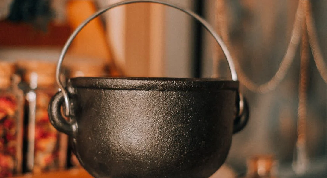 A black cast iron pot with a curved handle hanging in a warm kitchen.