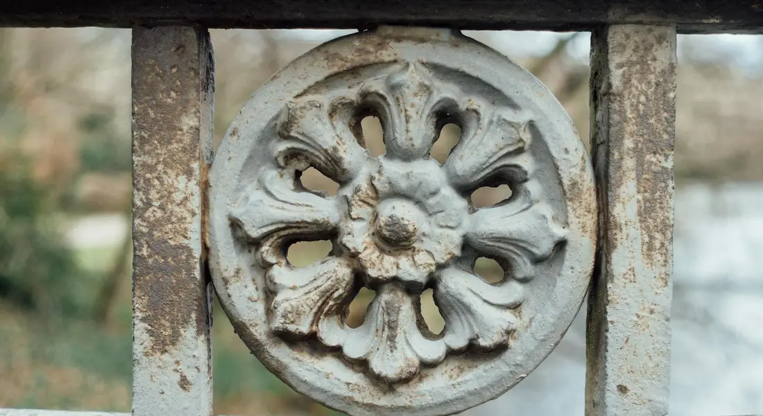 Close-up of a weathered cast-iron floral rosette on a railing with chipped white paint and rusty edges.