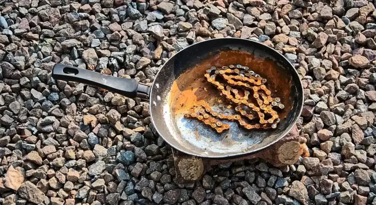 Rusty cast iron skillet resting on a bed of small rocks with visible corrosion inside the pan.