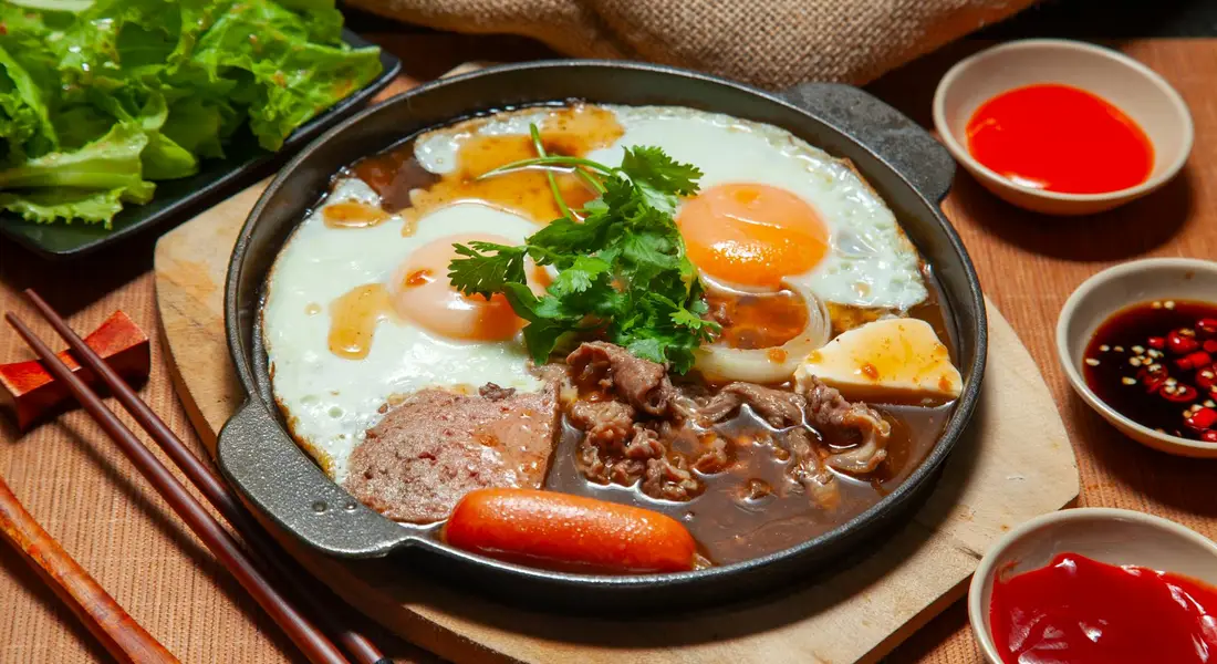 Cast iron skillet filled with fried eggs, sausage, bratwurst, and vegetables on a wooden board