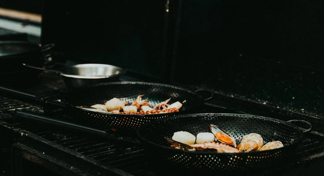 Two cast iron skillets on a stovetop with seafood pieces searing inside.