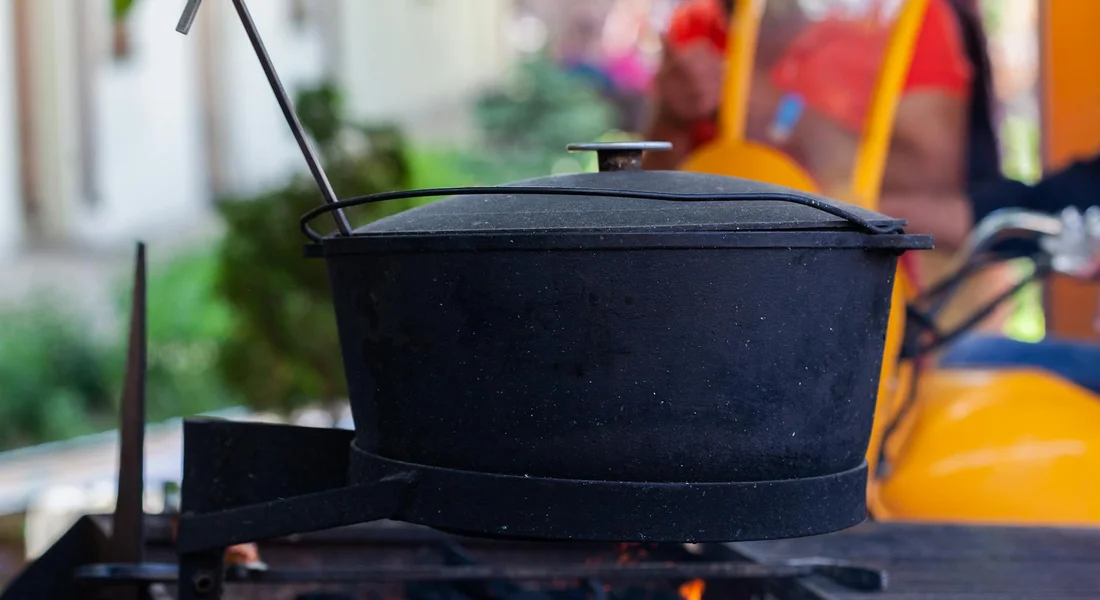 Cast iron pot with lid on a grill, with blurred people in the background