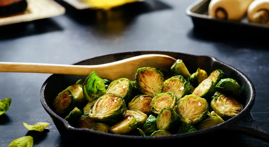 Cast iron skillet filled with roasted Brussels sprouts, with a wooden spatula resting on the edge.