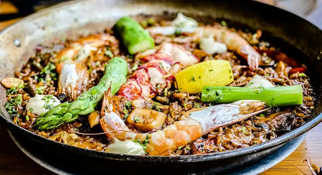 Cast iron skillet with shrimp, asparagus, onions, and lemon being sautéed; the pan’s interior shows a dark, seasoned surface.