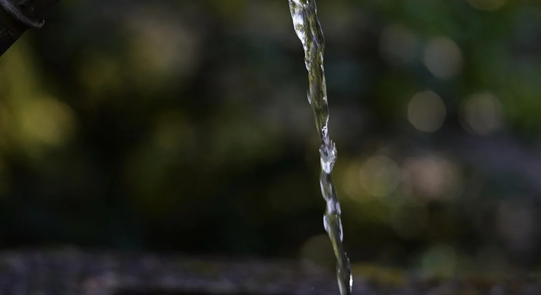 Close-up of a stream of water flowing from a faucet with a blurred natural background