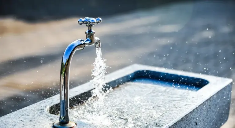 Close-up of a faucet with water flowing into an enamel-coated cast iron sink.