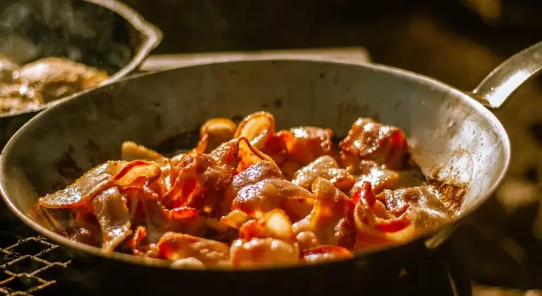 Cast iron skillet on a stovetop with sautéed bacon and onions, showing the skillet in use.