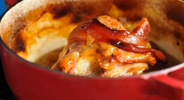 Close-up of a red cast-iron skillet with bubbling melted cheese and crispy toppings.