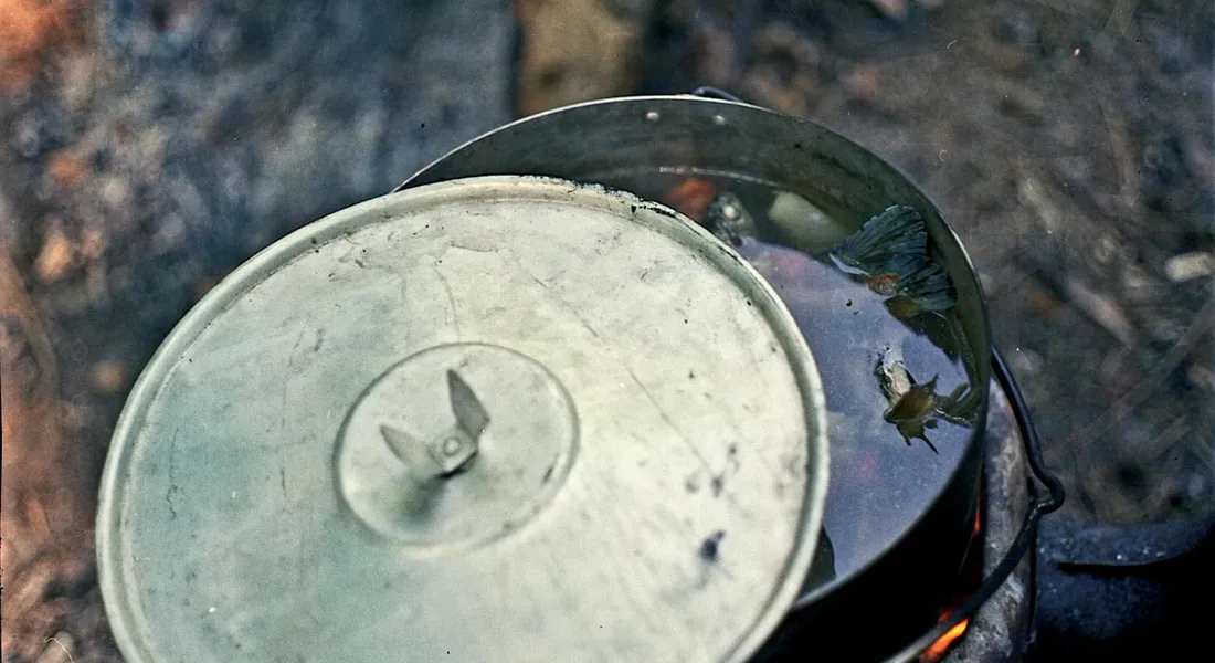 Cast iron skillet with lid resting on a campfire outdoors.