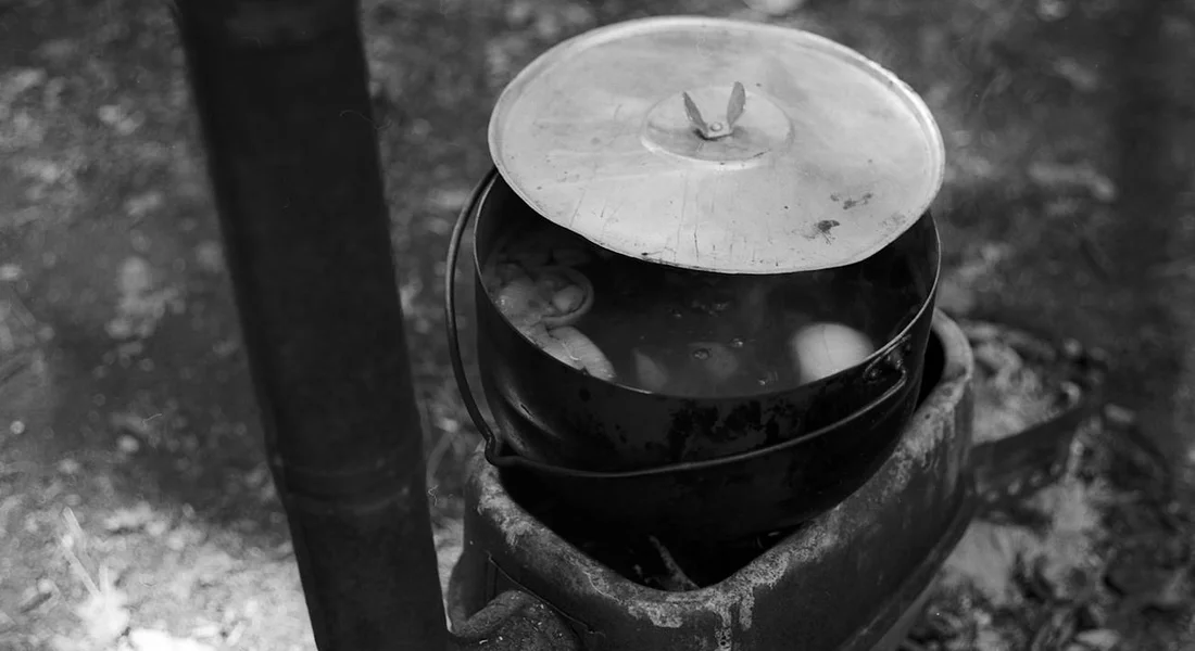 Cast iron cookware with lid resting on a small outdoor stove or hearth, illustrating readiness for proper storage.