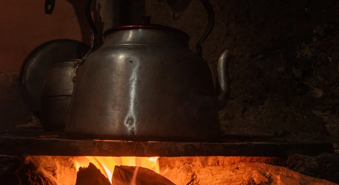 A kettle resting on a cast iron stove top with an orange glow from a fire underneath.