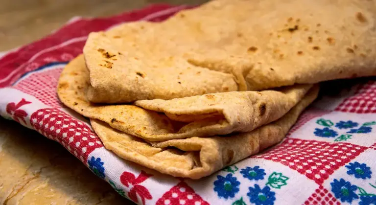 Stack of freshly baked flatbreads resting on a red and white patterned cloth