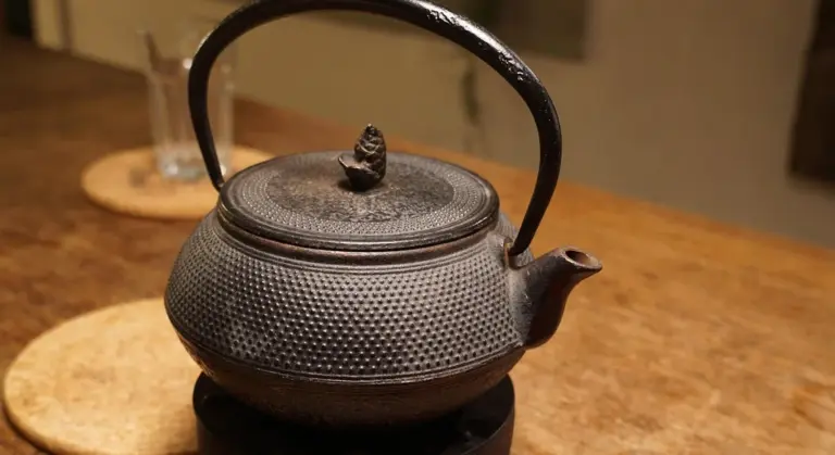 A textured cast-iron teapot with a curved handle and lid sits on a warm wooden surface.