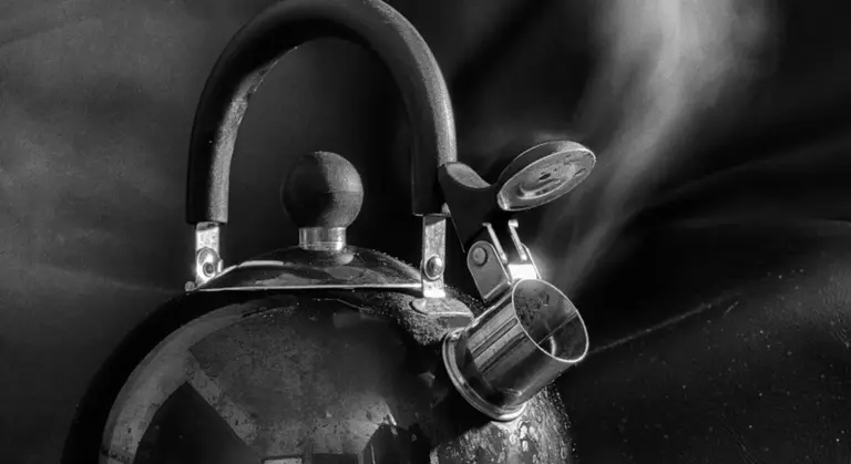Close-up of a traditional cast iron teapot with a curved handle and spout, shown in black and white.