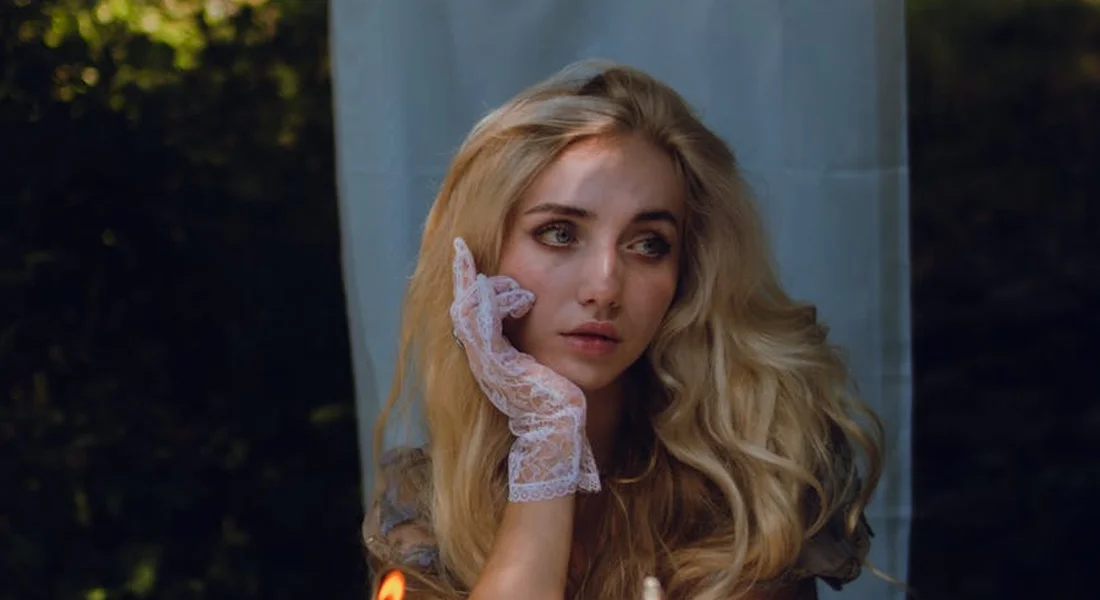 Portrait of a woman with long blonde hair wearing a lace glove, outdoors.