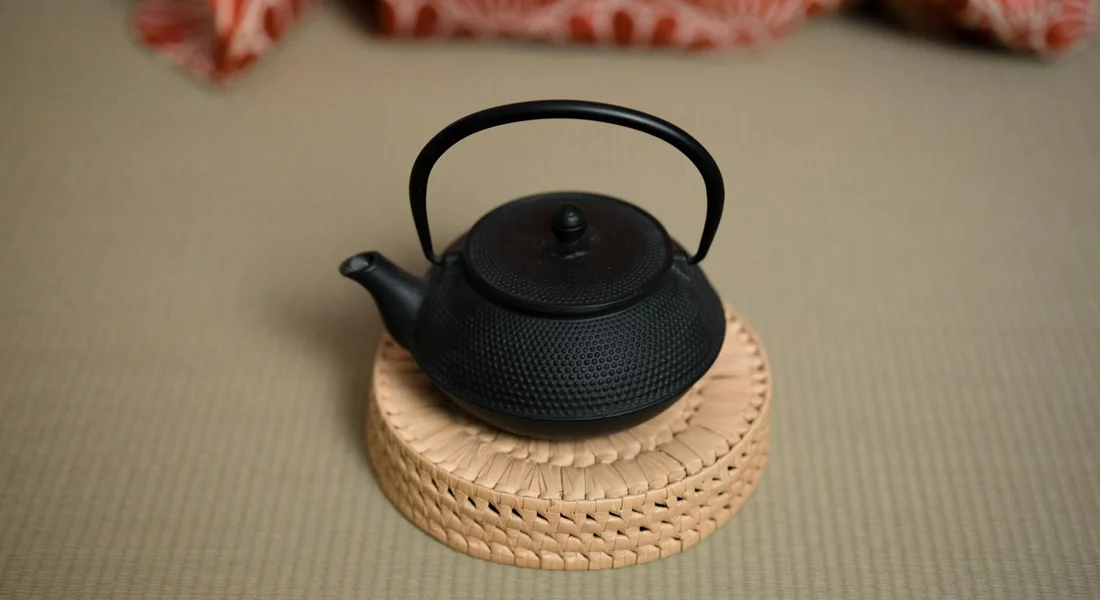 Small black cast iron teapot on a woven round trivet.
