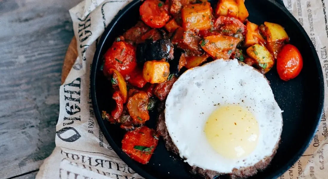 Cast-iron skillet with roasted vegetables and a fried egg, showing how food can stick during cooking.