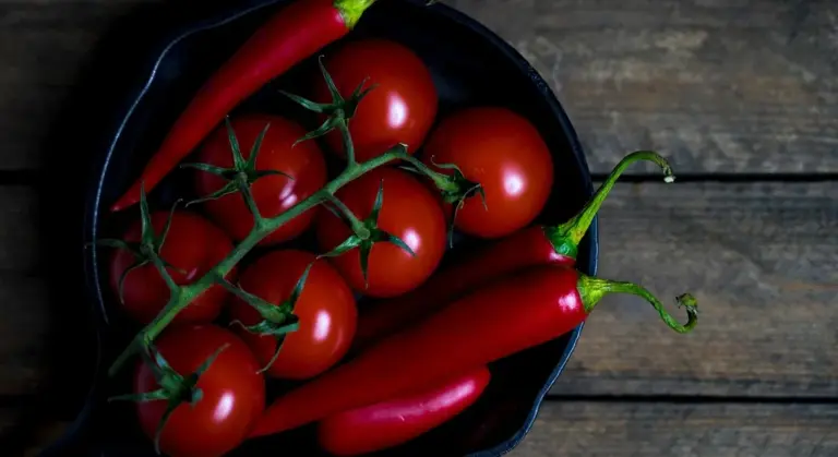 Red chili peppers and vine tomatoes in a black cast iron skillet on a wooden surface.