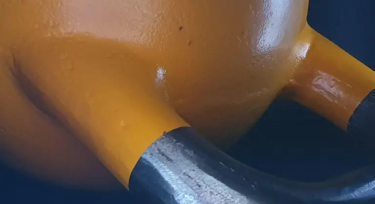 Close-up of enameled cast iron cookware with an orange body and dark metal handles.