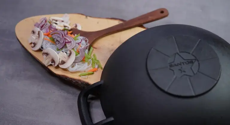 A wooden cutting board with sliced mushrooms, onions, and peppers next to a black cast iron skillet.